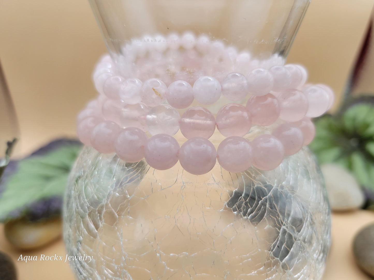 Stack of Rose Quartz beaded bracelets on a glass surface with 'Aqua Rocks Jewelry' branding.