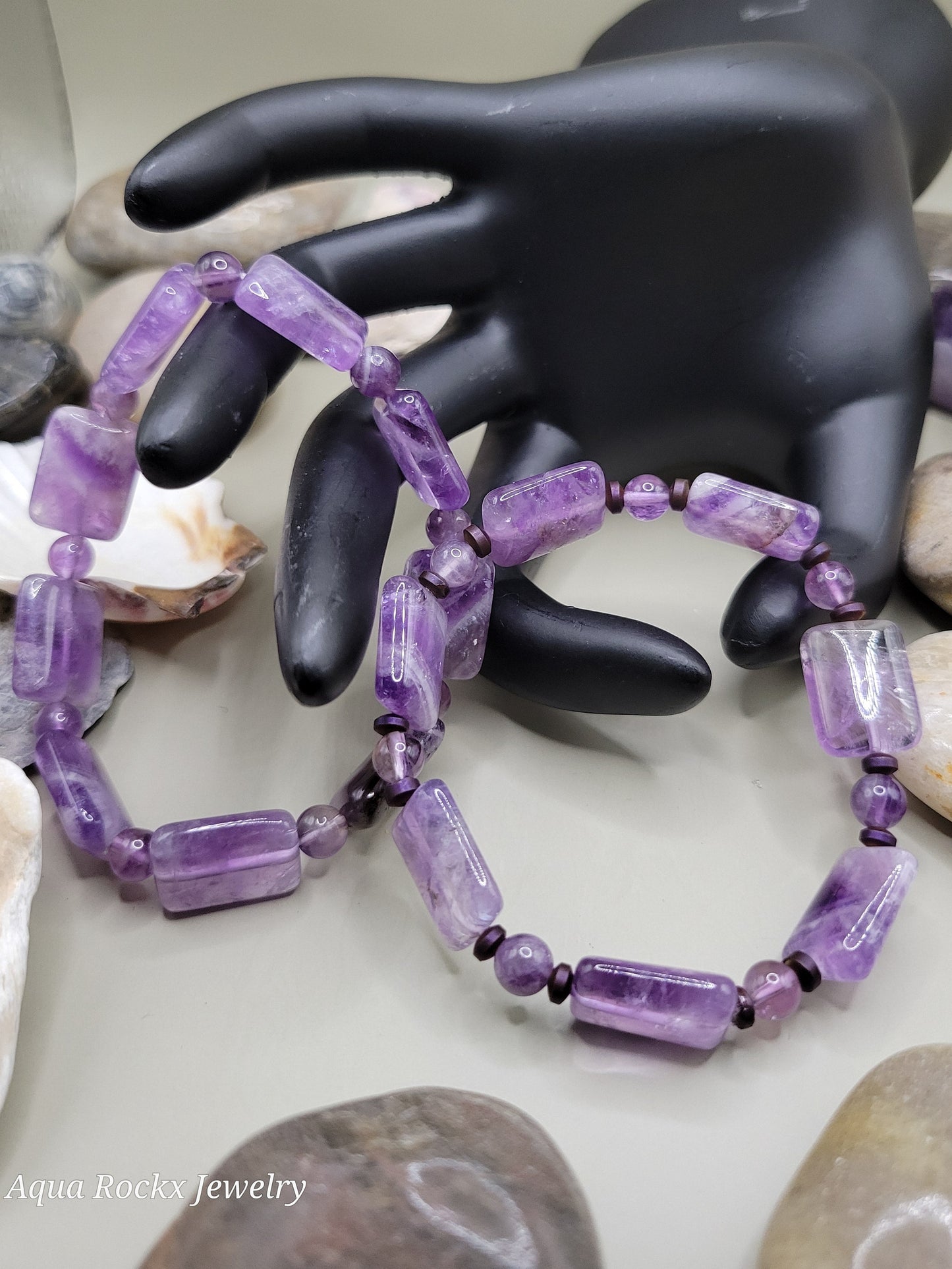Purple beaded bracelet on a black mannequin hand with seashells in the background
