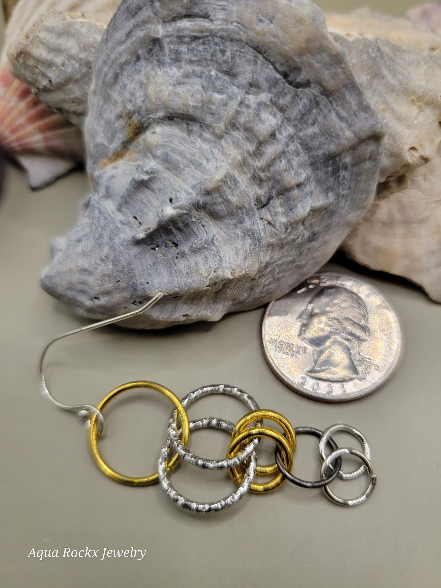Jewelry with rings on a rock and coin background, featuring 'Aqua Rockx Jewelry'.