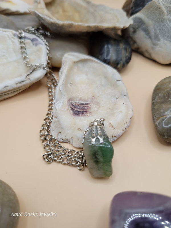 Silver chain necklace with a green stone pendant on pebbles