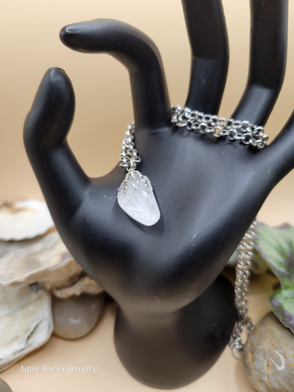 Silver chain necklace with a white pendant on a black mannequin hand against a beige background.