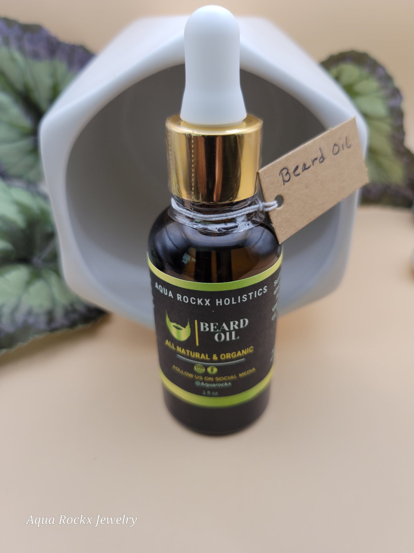 Bottle of beard oil with dropper on a white container, surrounded by green leaves.