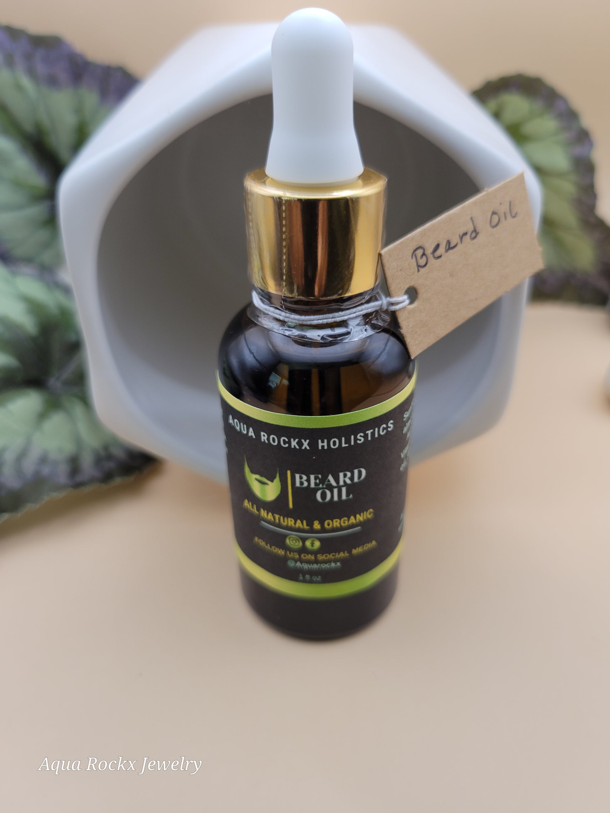 Bottle of beard oil with dropper on a white container, surrounded by green leaves.