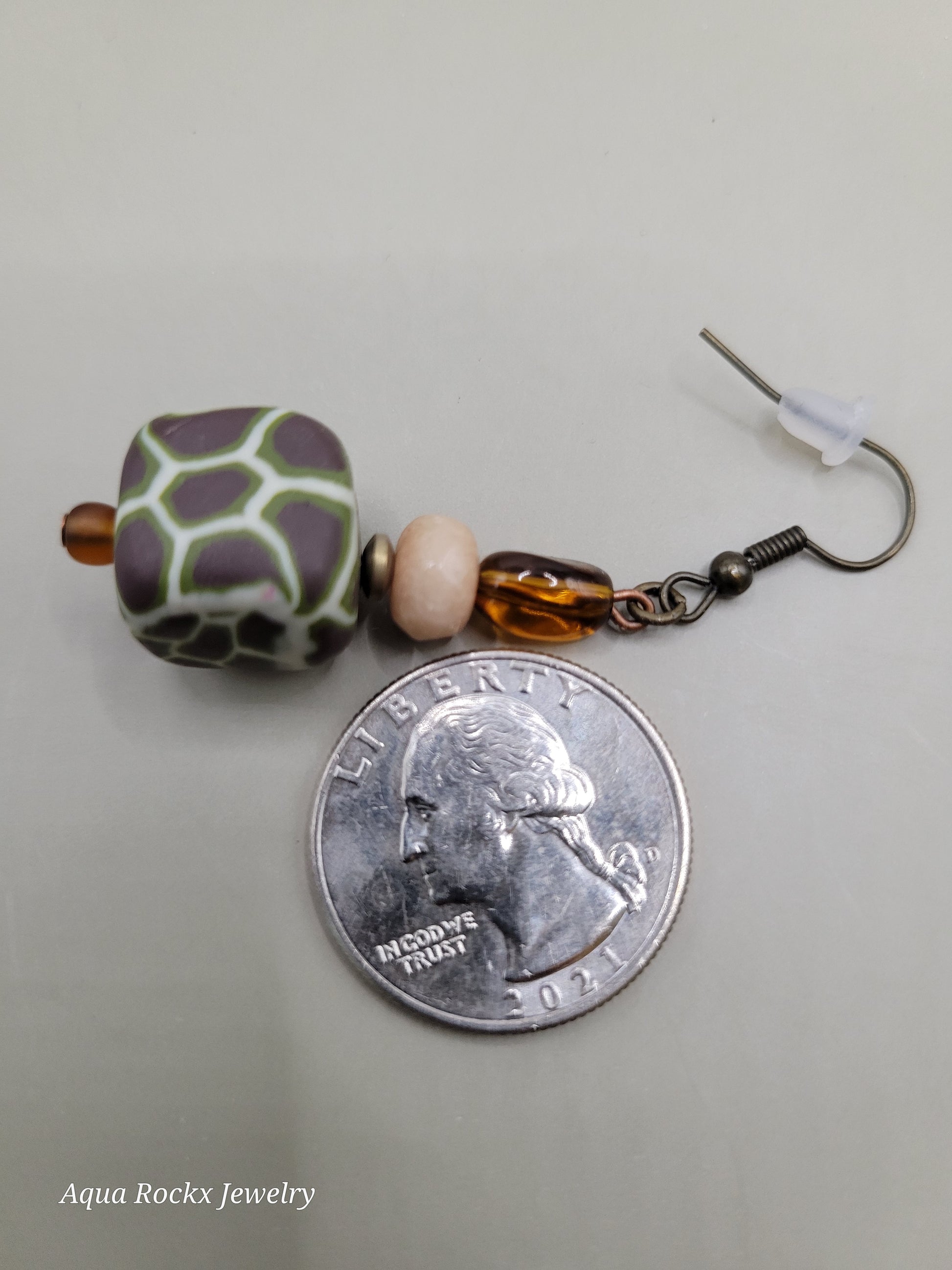 Earrings with beads on a quarter for scale on a gray background