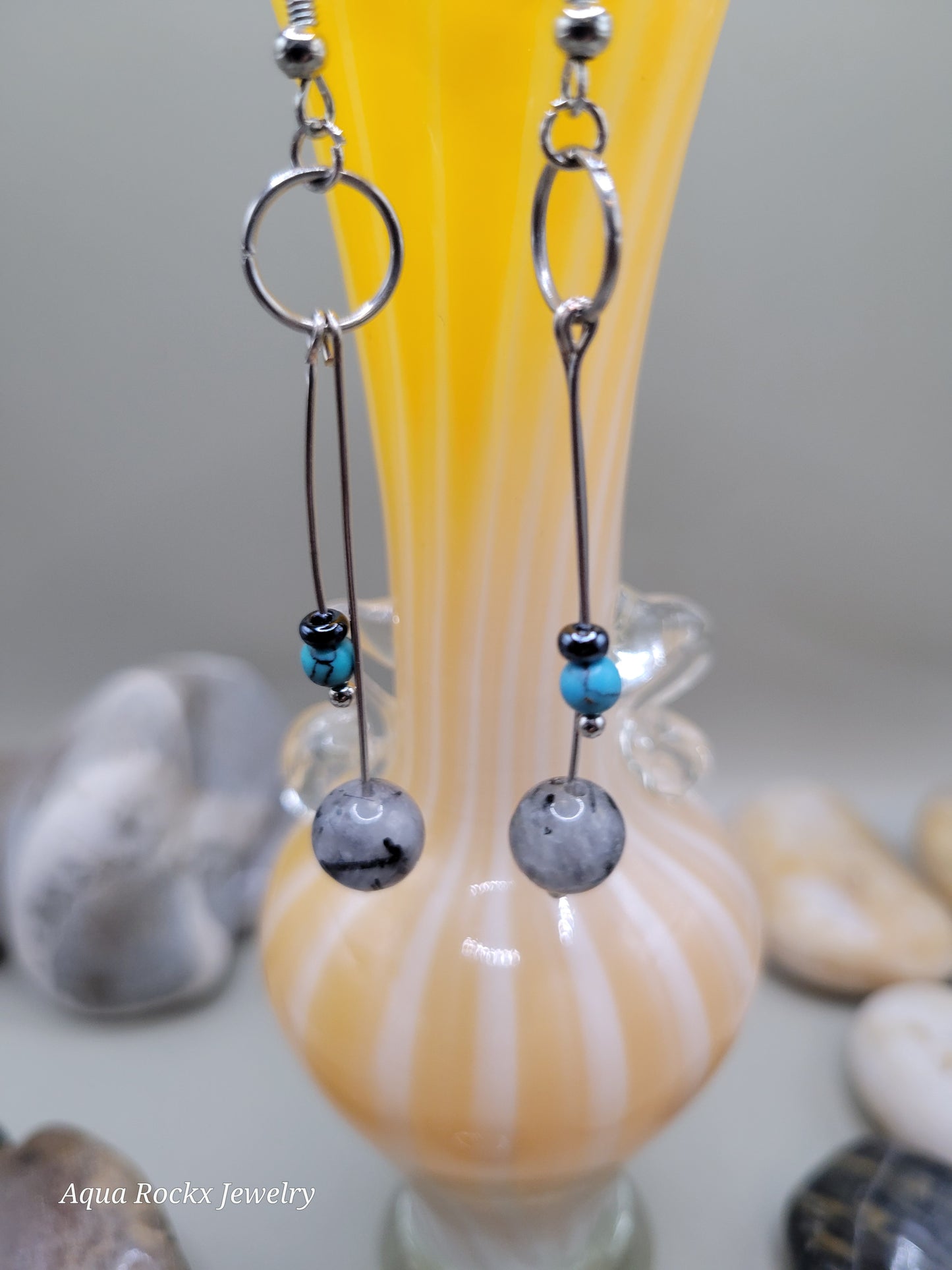 Close-up of earrings with beads on a shell background, brand 'Aqua Rockx Jewelry' visible.