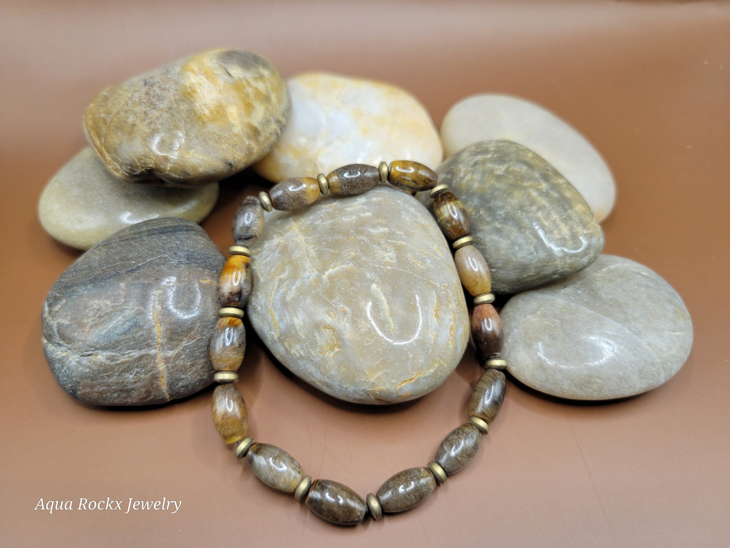 Bracelet with natural stone beads on a pile of stones with 'Aqua Rockx Jewelry' branding.