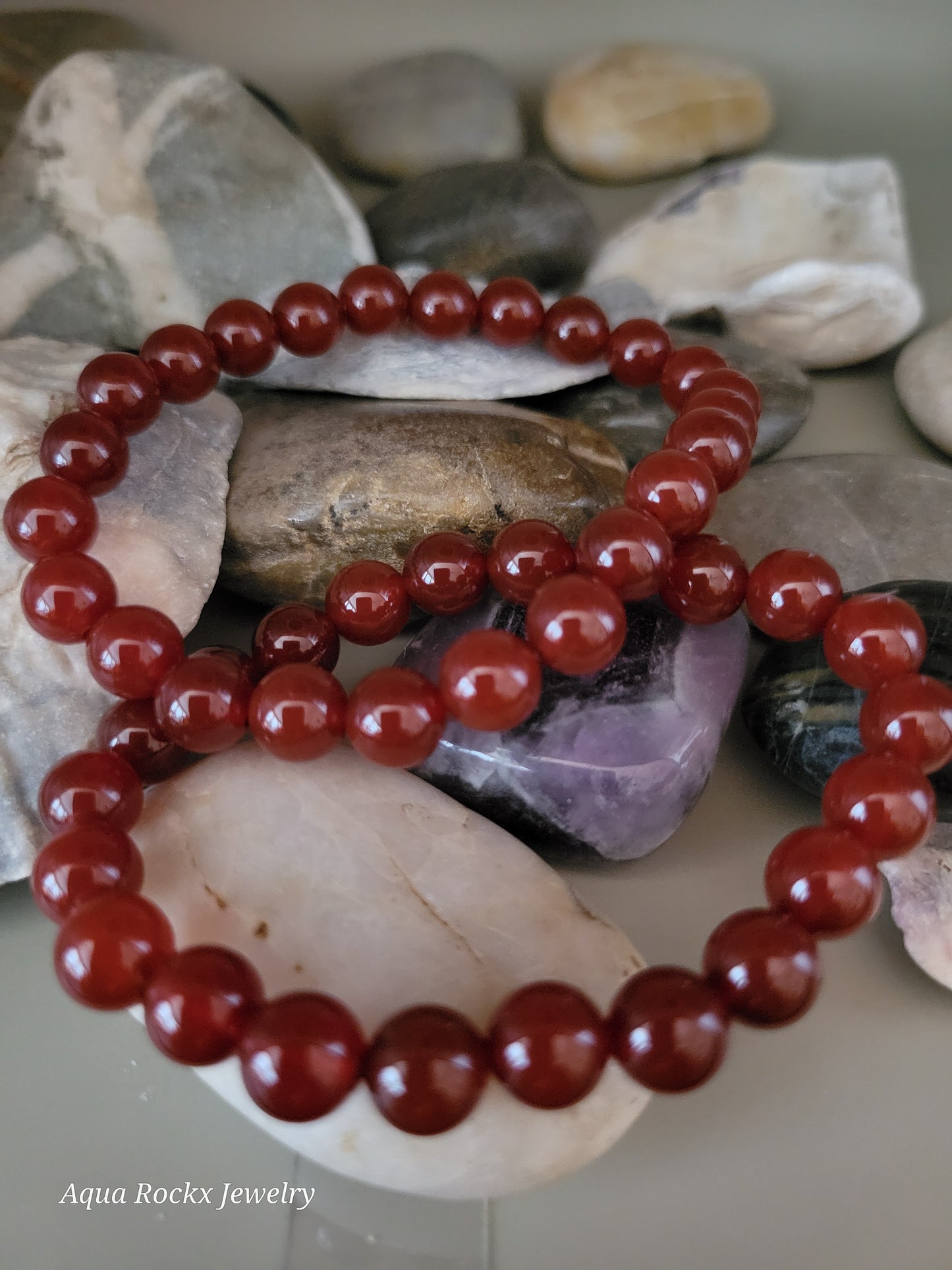 Deep orange beaded bracelet on a background of pebbles
