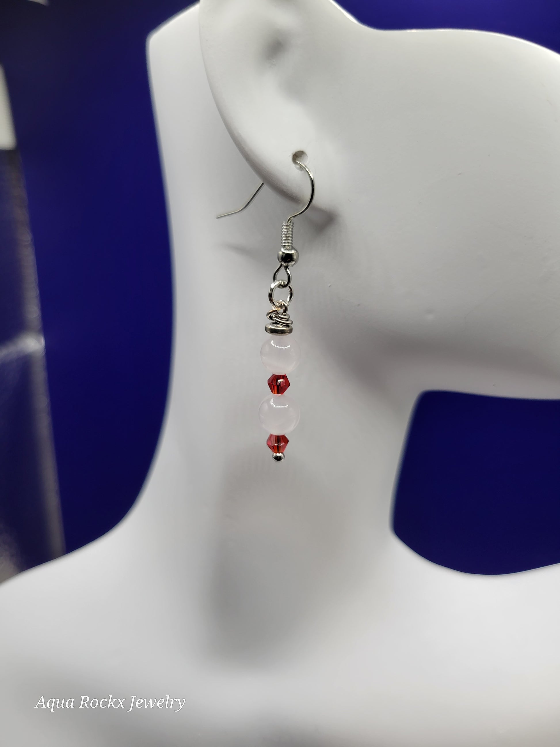 White quartz, silver hematite, red glass accent earring on a mannequin ear with a blue background