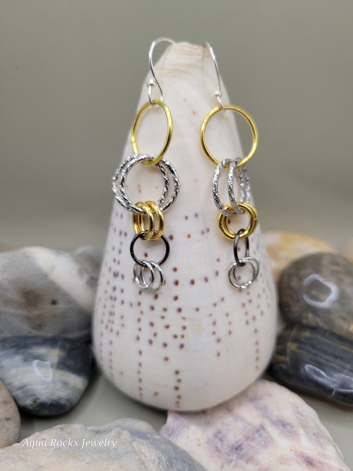 Two silver and gold bracelets on a stack of seashells.
