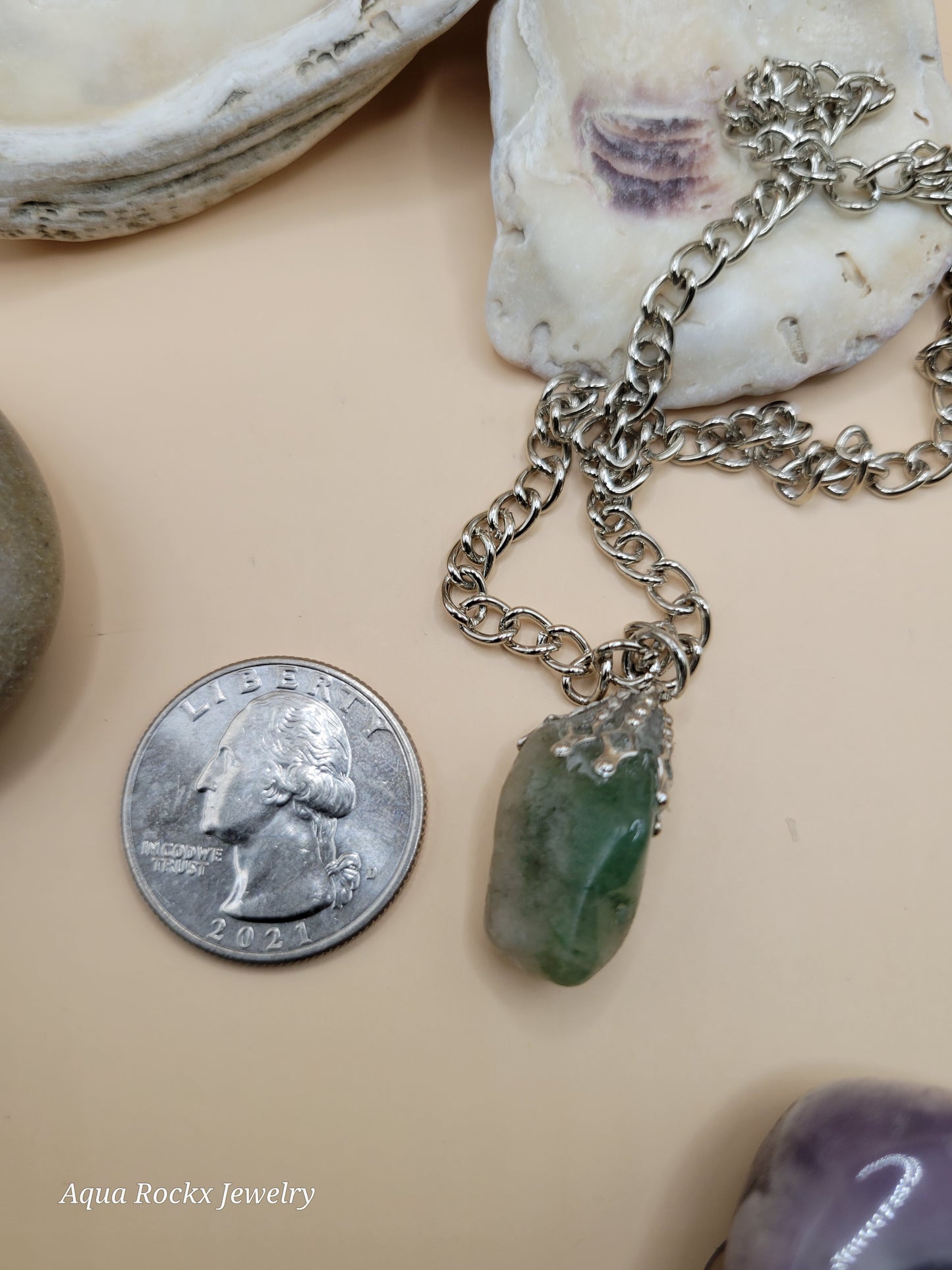 Necklace with a pendant next to a quarter on a beige surface
