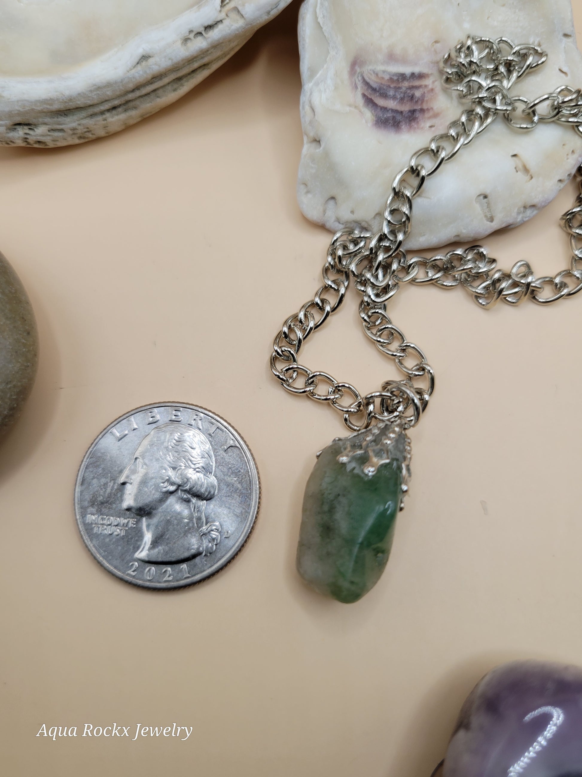Necklace with a pendant next to a quarter on a beige surface