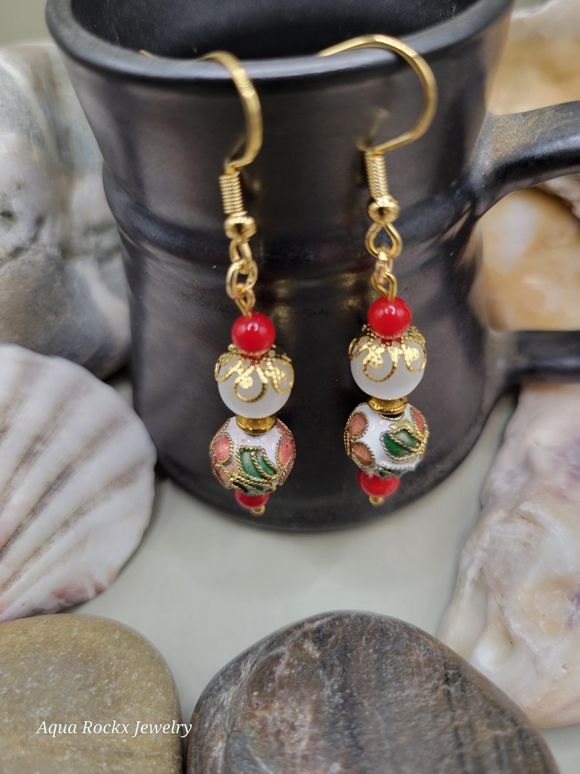 Pair of gold earrings with red and white beads on a stone surface