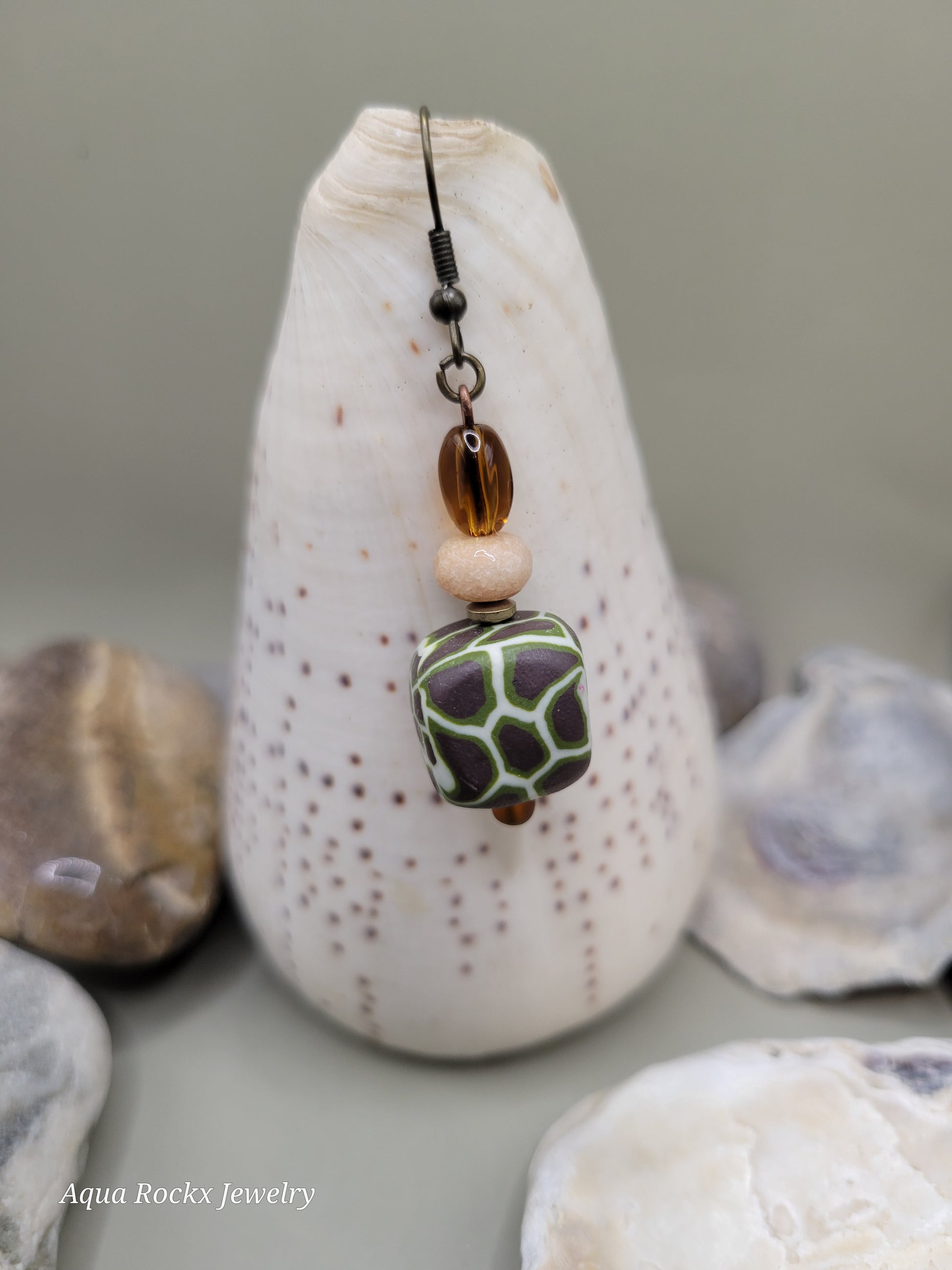 Jewelry with a green and brown bead on a shell with seashells in the background