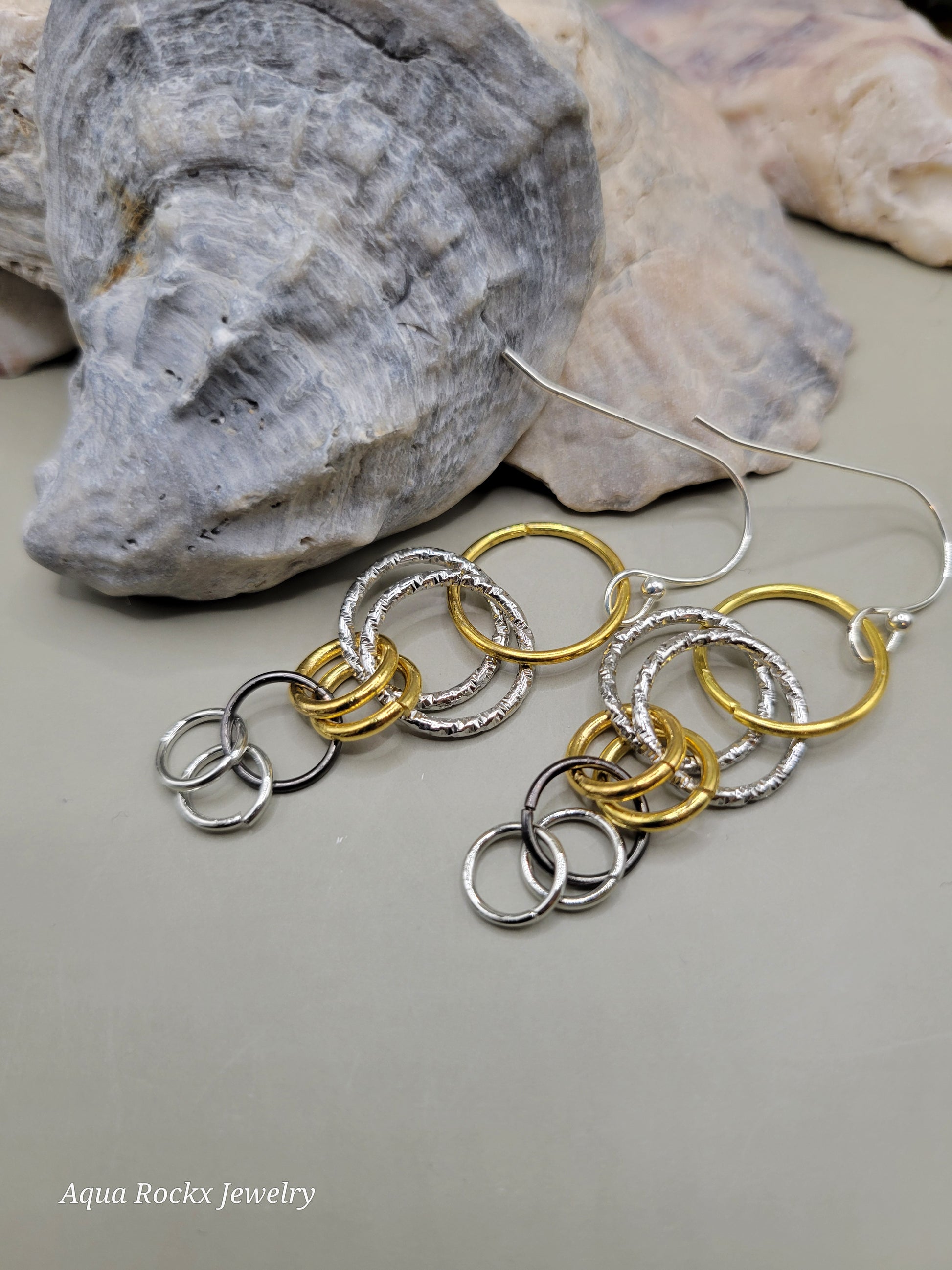 Pair of gold and silver hoop earrings on a neutral background with 'Aqua Rockx Jewelry' branding.