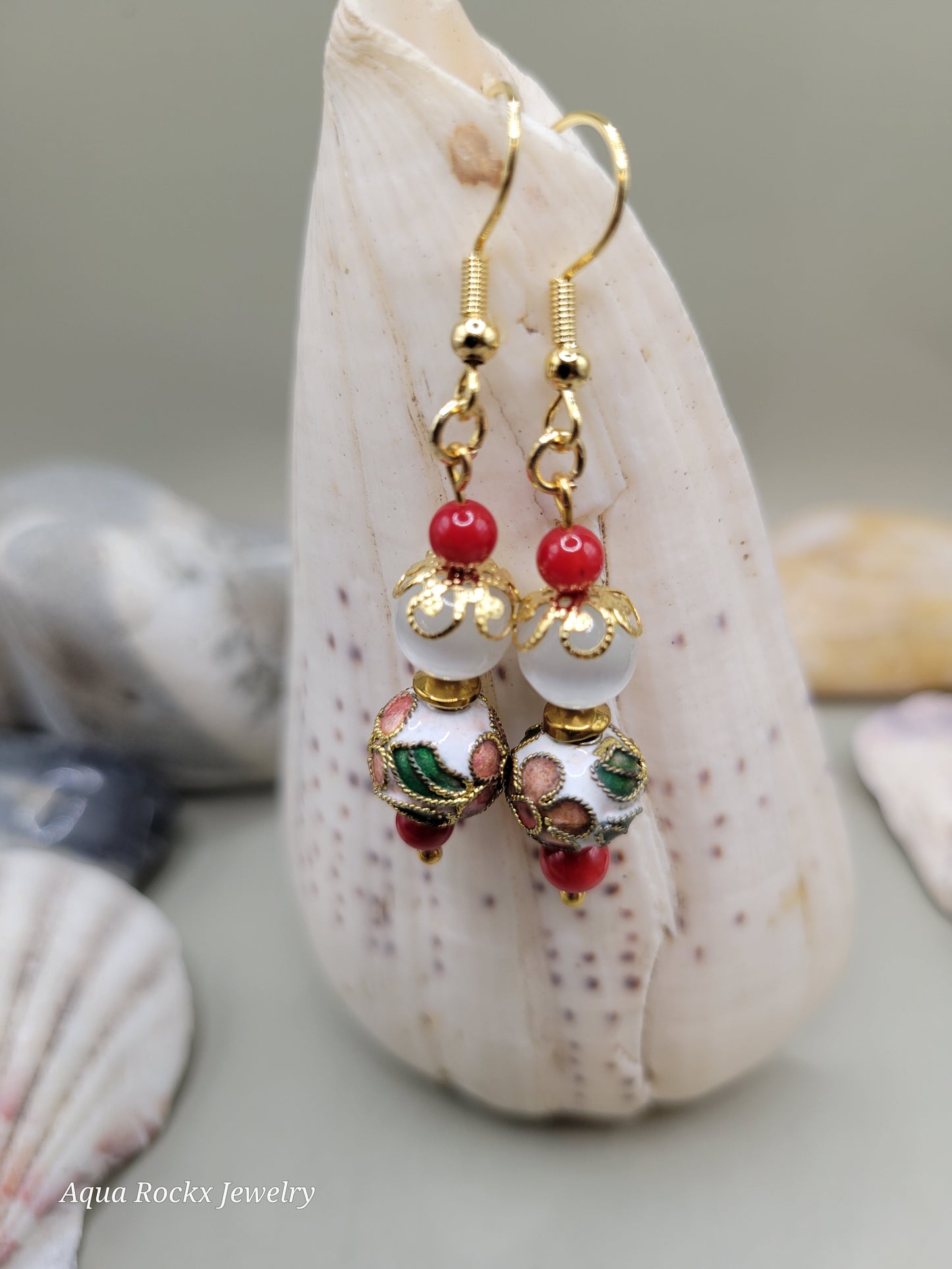 Gold earrings with red and green beads on a shell