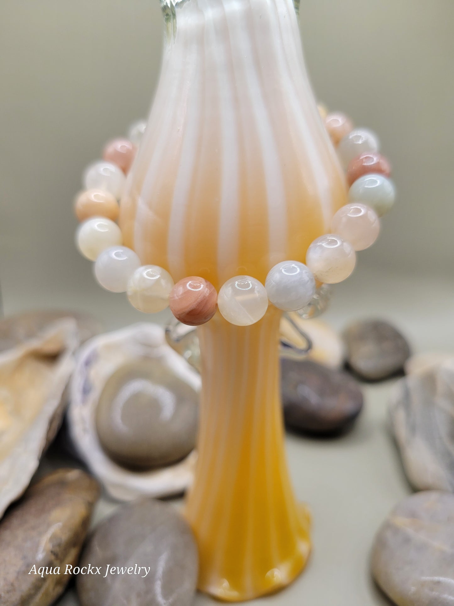 Close-up of a beaded bracelet with a shell and stones in the background