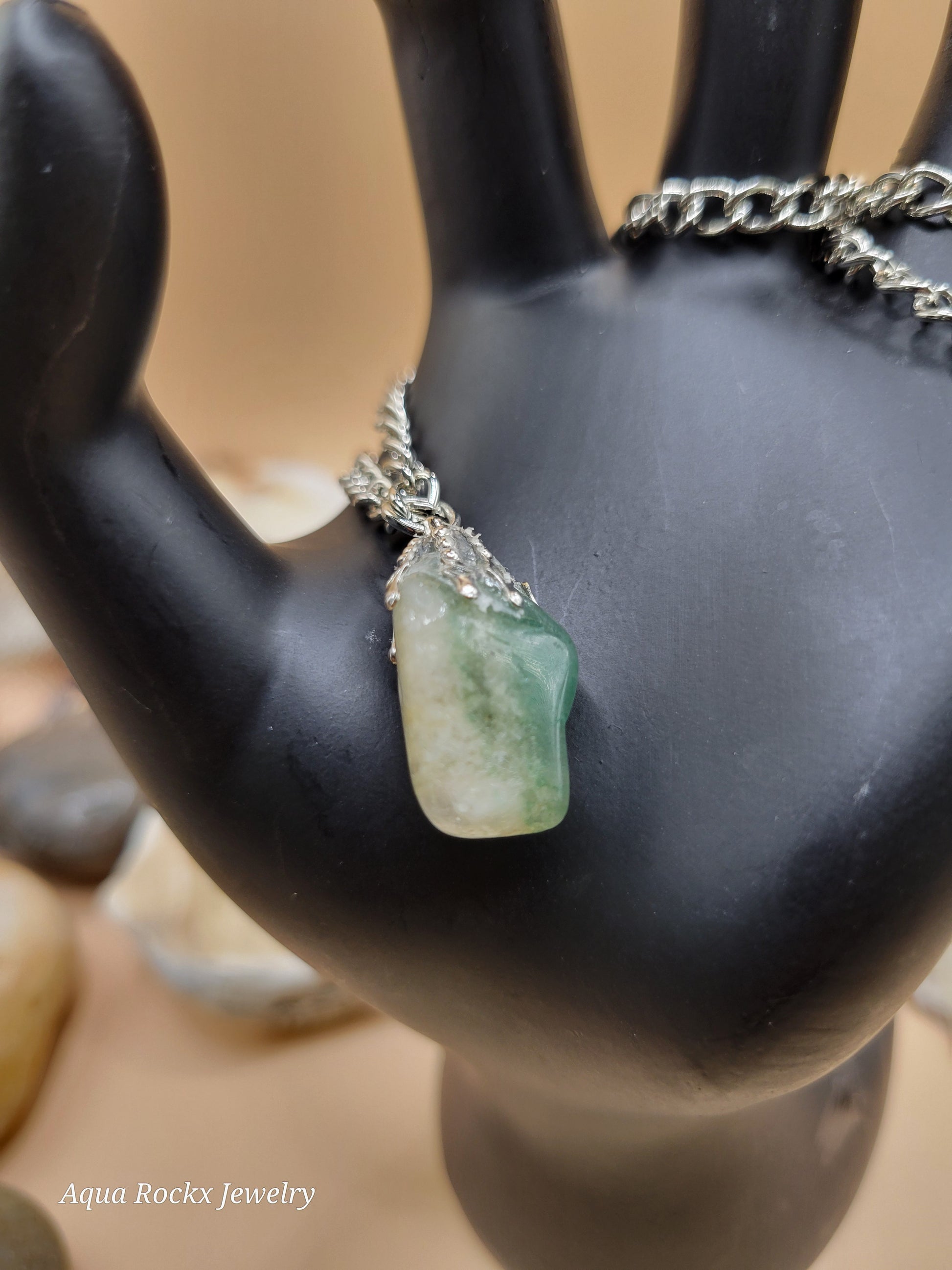Jewelry with a green stone and silver chain on a black stand.