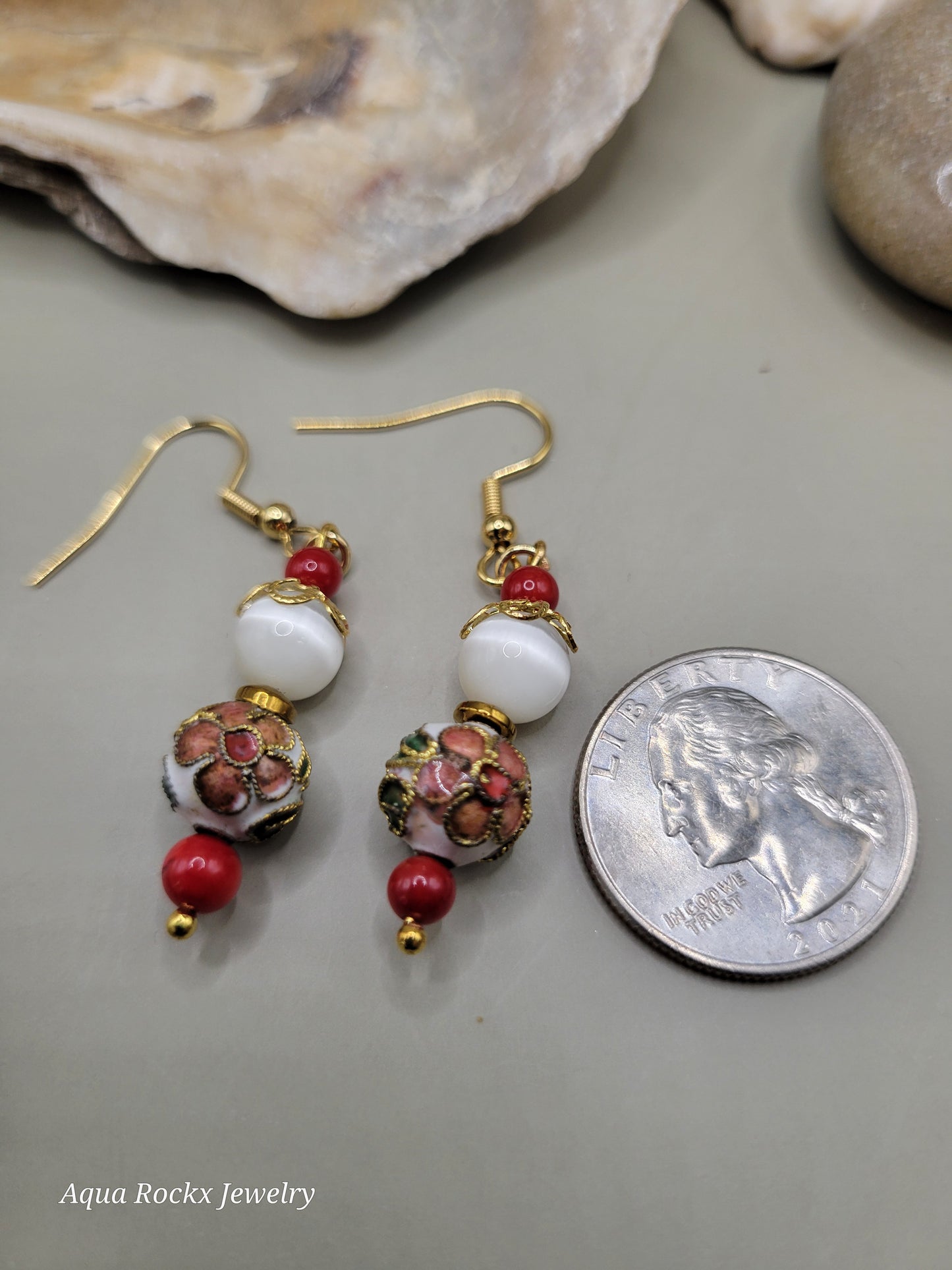 Pair of earrings with red and white beads on a gray surface next to a quarter for scale.