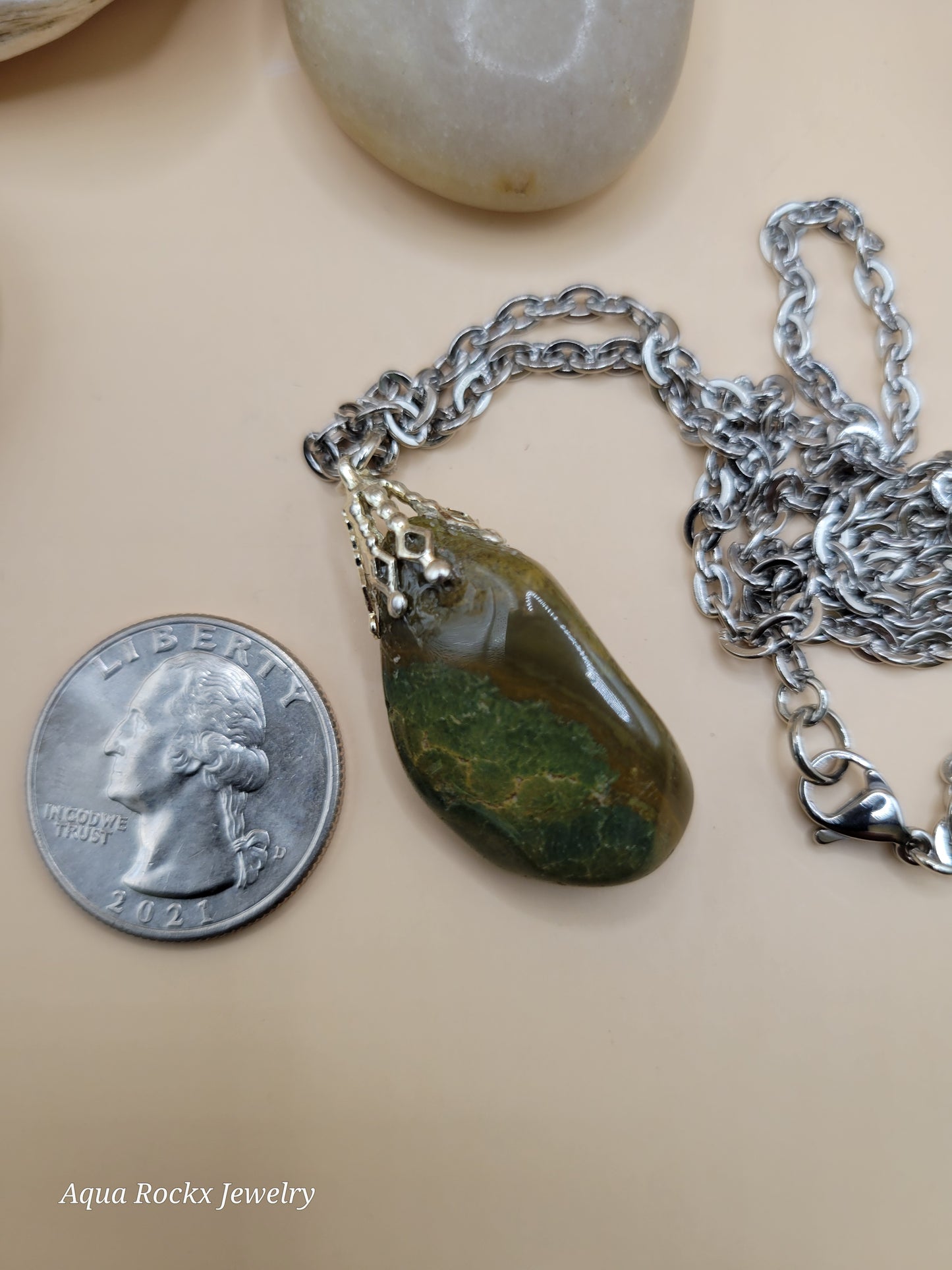 Necklace with a green stone pendant next to a quarter on a beige background
