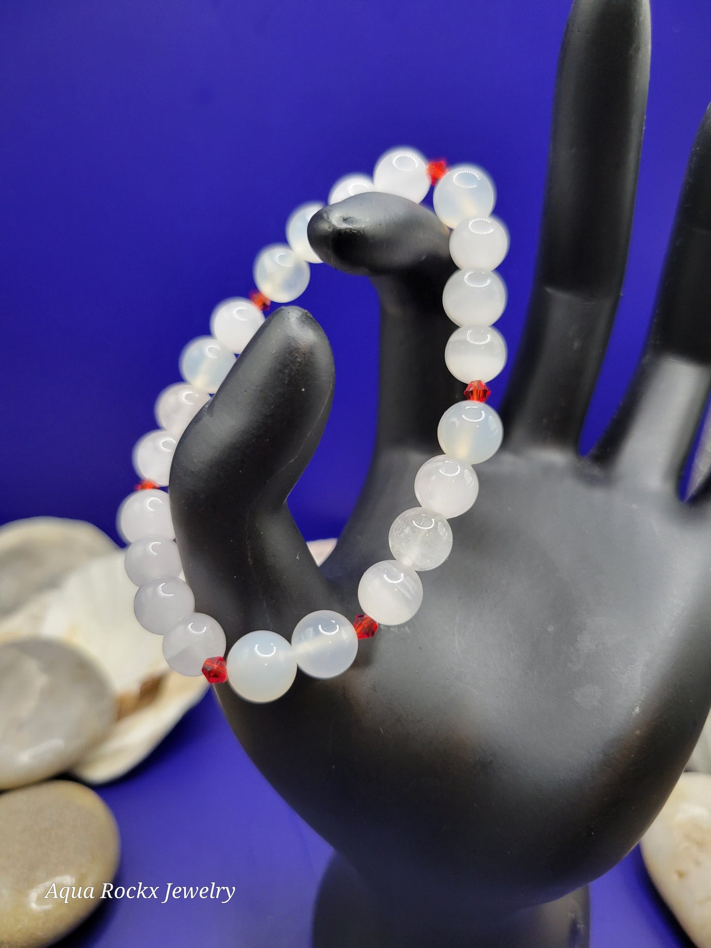 White beaded bracelet with red accents on a black mannequin hand against a blue background