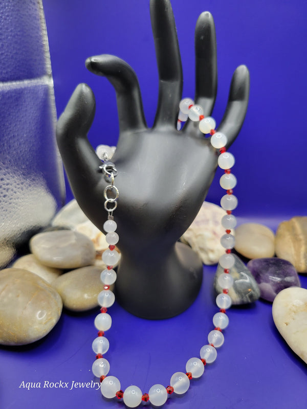 Black mannequin hand holding a white and red beaded necklace.