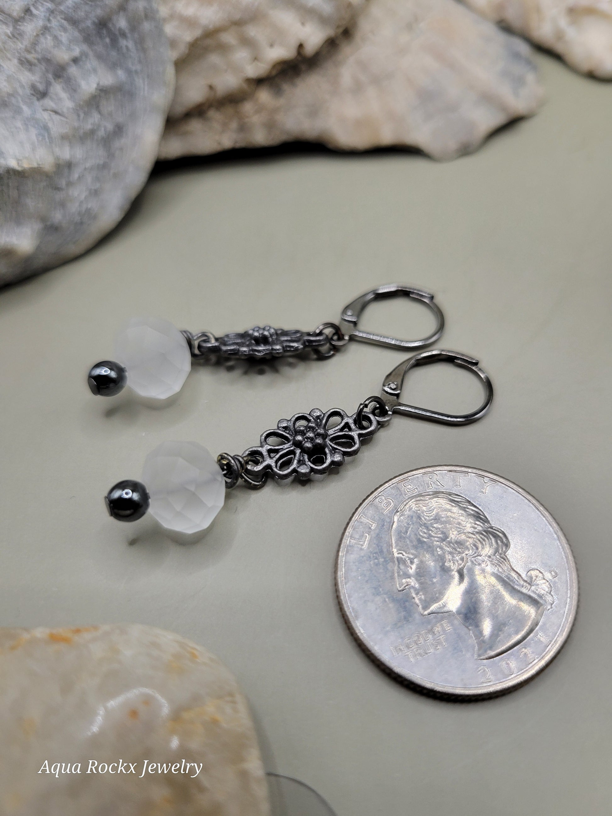 Pair of earrings with white quartz and black beads next to a quarter on a stone surface.