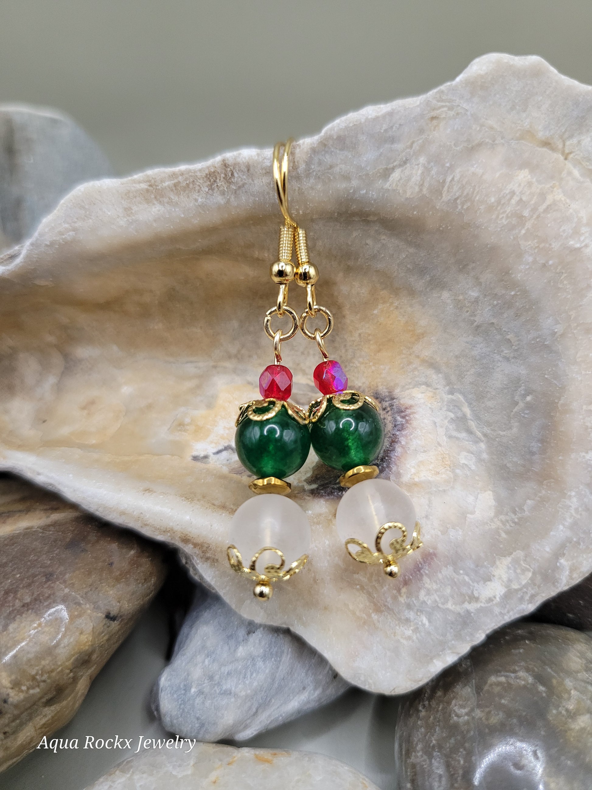 Gold earrings with green and red beads on a rock background