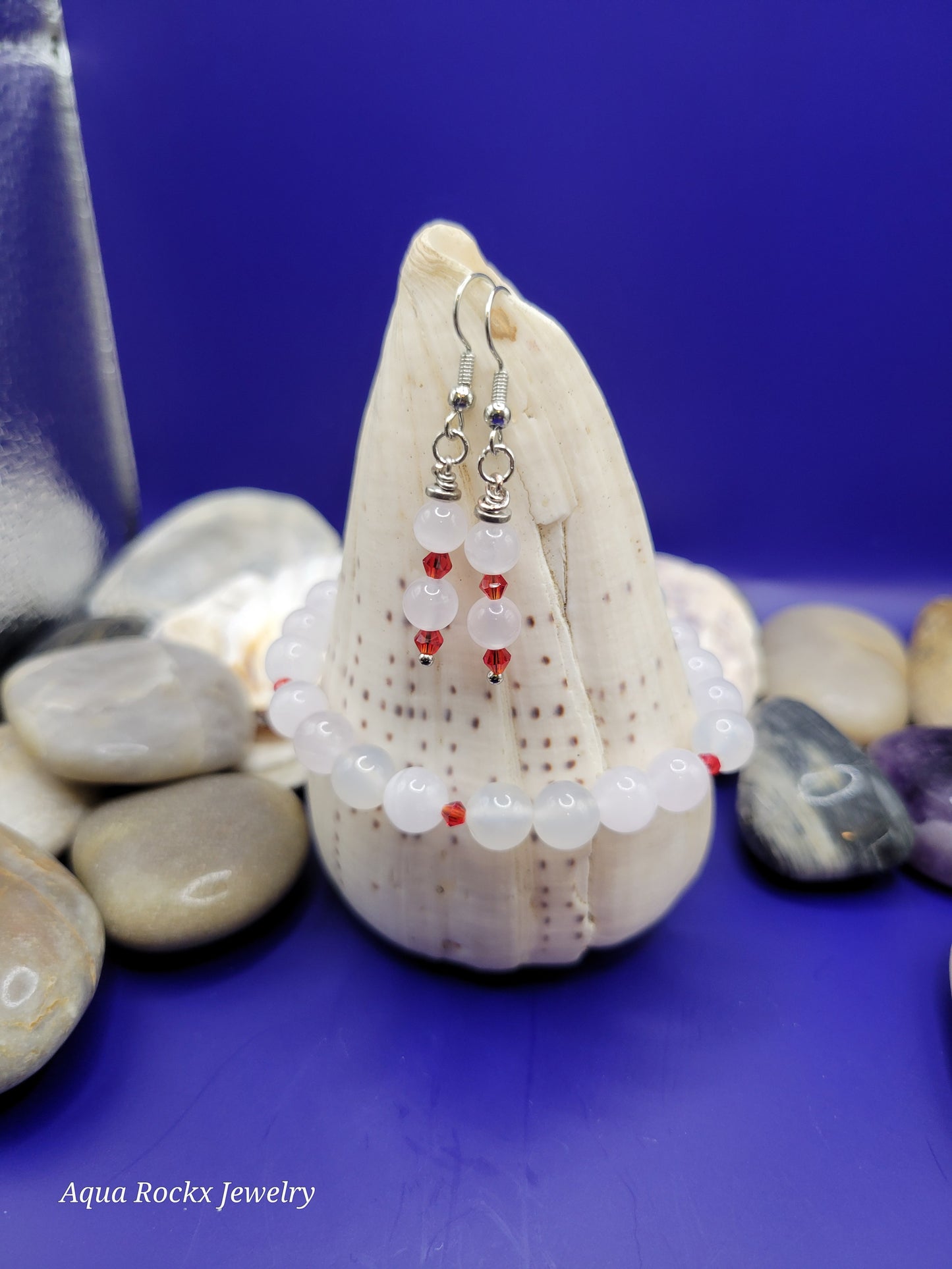 White quartz earrings and bracelet on a shell with pebbles and a blue background